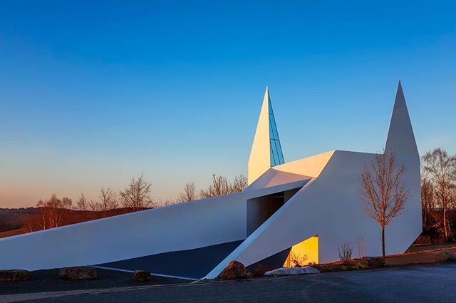 A modern white building with unique architectural design stands against a clear blue sky.