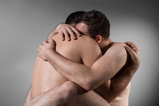 Two men share a tender embrace in a studio setting, conveying warmth and intimacy.