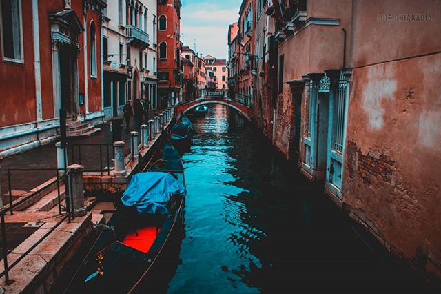 A canal in Venice, Italy is framed by historic buildings and a small bridge, creating a scenic cityscape.