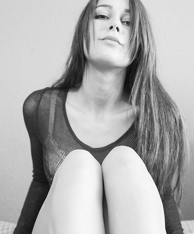 A woman with long hair sits with her knees up in a black and white portrait.