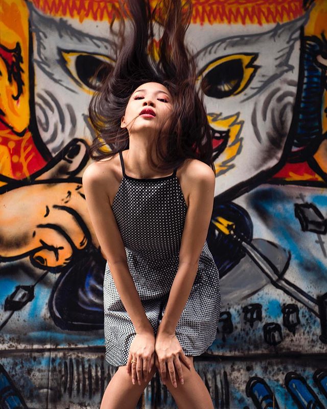 A woman in a dress poses in front of colorful graffiti, creating an urban editorial shot perfect for social media.