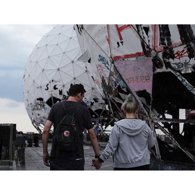 A couple holds hands while exploring a graffiti-covered radar dome, captured in a candid and relaxed travel photo.