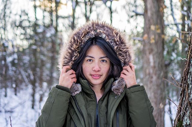 A woman in a fur-lined coat enjoys a peaceful walk in a snowy forest.