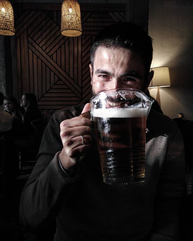 A happy man raises a large mug of beer in a cozy, warmly lit bar. Cheers!