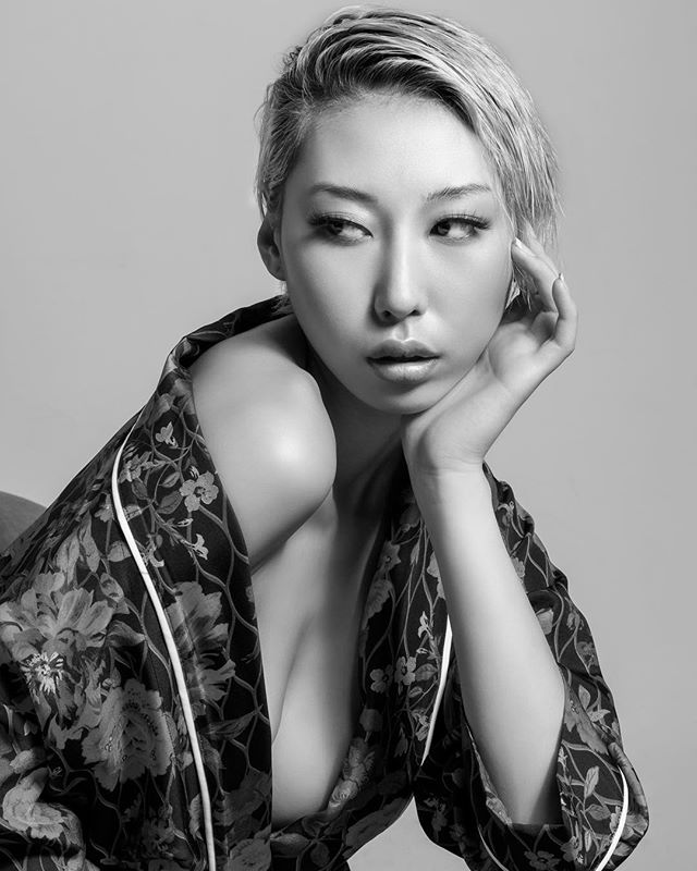 A monochrome portrait of an Asian woman in a floral robe, exuding a dreamy and sensual mood in a studio setting.