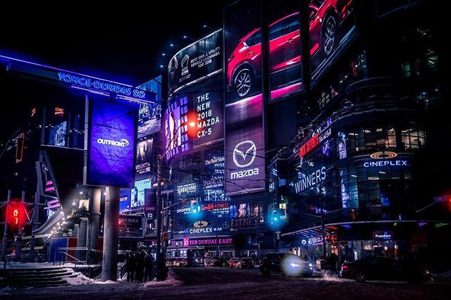 A vibrant night cityscape featuring illuminated advertisements and bustling urban activity.