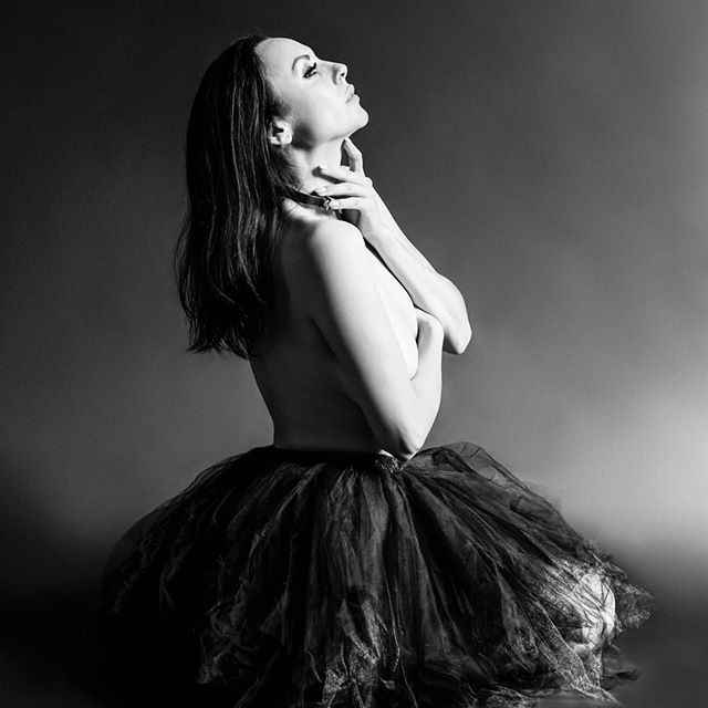 A ballerina poses in a tutu in a fine art, black and white studio shot, showcasing emotion and sensuality.