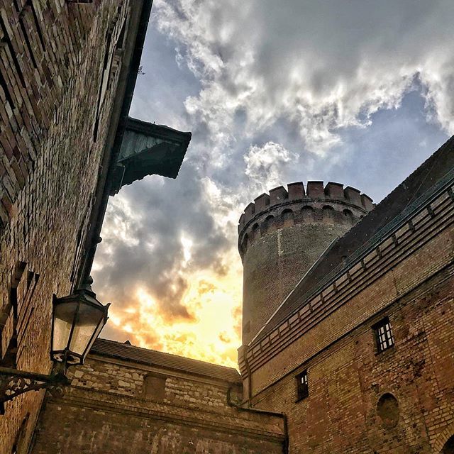 A brick tower rises amongst buildings under a cloudy sky, showcasing historical architecture and urban scenery.