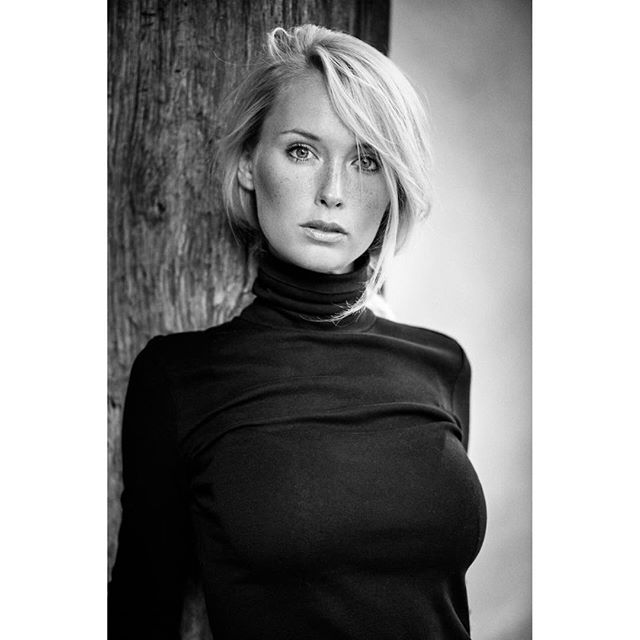 A black and white portrait of a woman with blonde hair wearing a black turtleneck. 