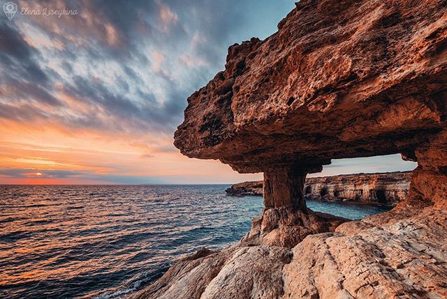 A scenic view of rock formations and the ocean during a vibrant sunset on the coastline.