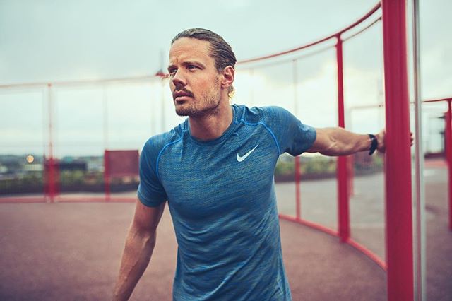 An athletic man wearing Nike apparel, leans against a red railing on an outdoor sports court.