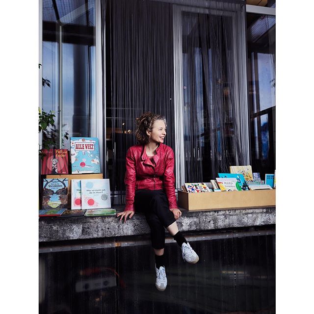 A woman sits surrounded by children's books, creating a welcoming scene at a bookstore.