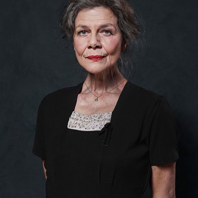 Portrait of an older woman with red lipstick and grey hair wearing a black dress.
