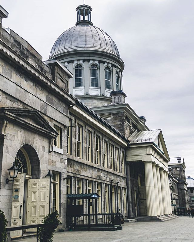A classical building with a dome and large columns under a cloudy sky in an urban setting.