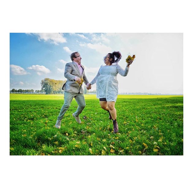 A cheerful couple jumps and celebrates in a grassy field on a sunny day.