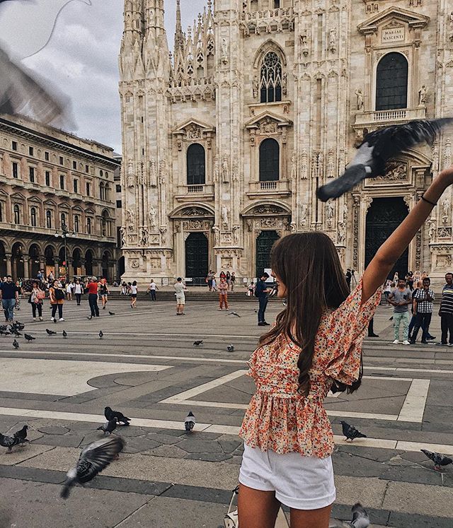 A woman feeds pigeons in Piazza del Duomo, Milan, with the Duomo di Milano in the background.