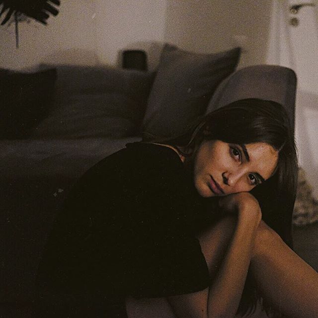 A brunette woman sits pensively in a softly lit room, embracing a mood of quiet introspection.