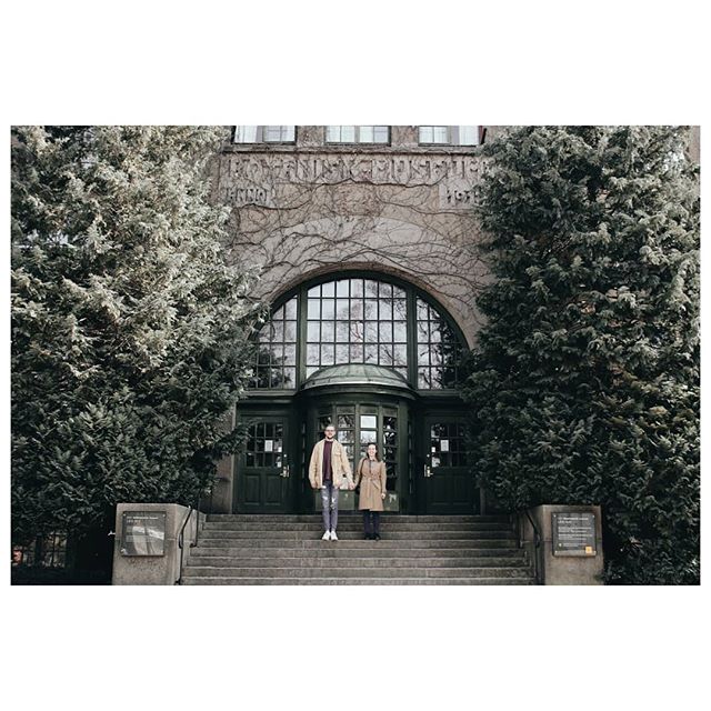 A couple stands on steps in front of an old building surrounded by trees in a vintage style, perfect for advertising.
