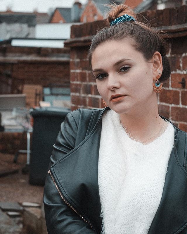A woman with a leather jacket and scrunchie poses on a rooftop.