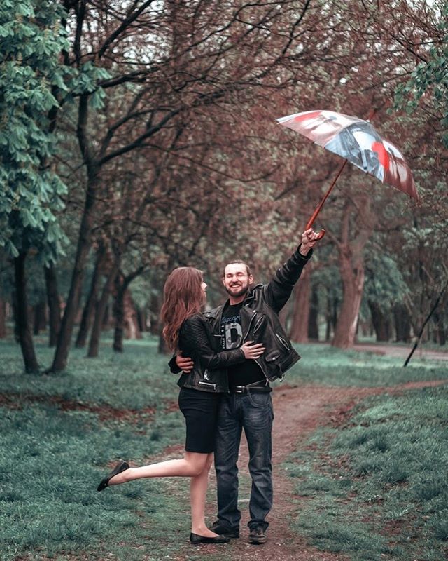 A smiling couple embraces under an umbrella in a park, perfect for romantic themes.