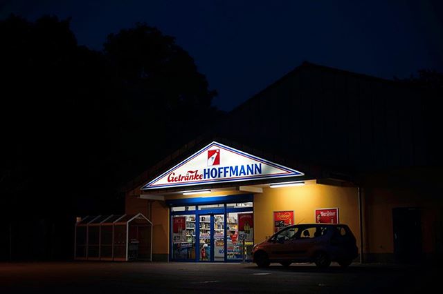 A Getränke Hoffmann store illuminated at night, creating a warm and inviting scene.