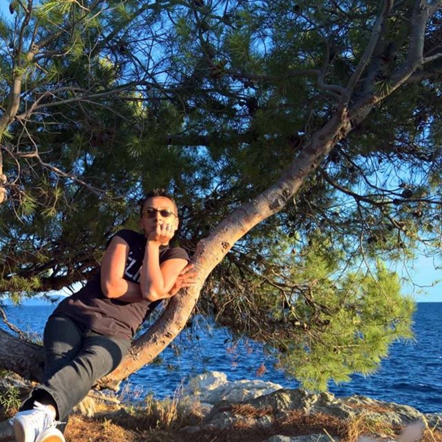 A woman relaxes on a tree branch overlooking the ocean on a sunny day.