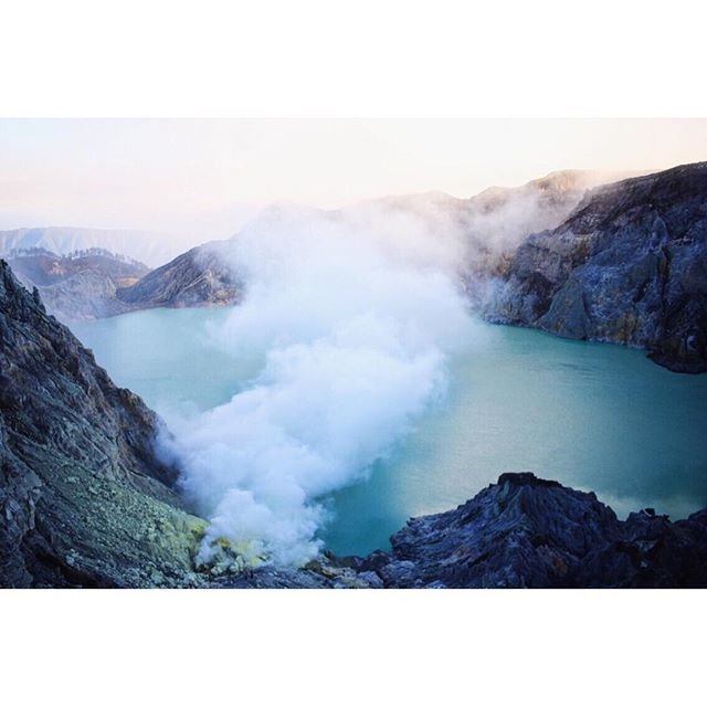 Ijen volcano's turquoise crater lake surrounded by mountains and sulfur smoke creates a mysterious, serene landscape.