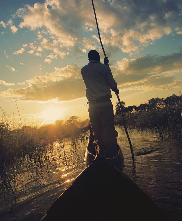 A lone boater navigates a tranquil river at sunset, casting a striking silhouette against the sky.
