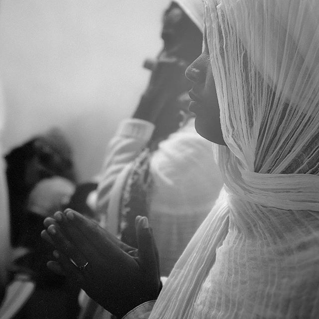 A woman in a veil prays, her hands clasped in devotion. Black and white image evokes serenity and reflection.