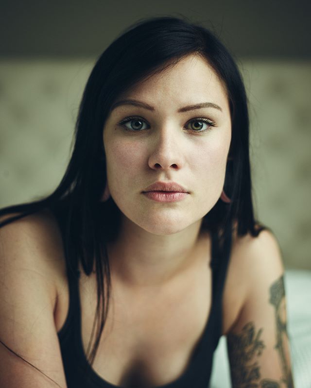 A portrait of a woman with dark hair looking directly at the camera in a naturally lit indoor setting.