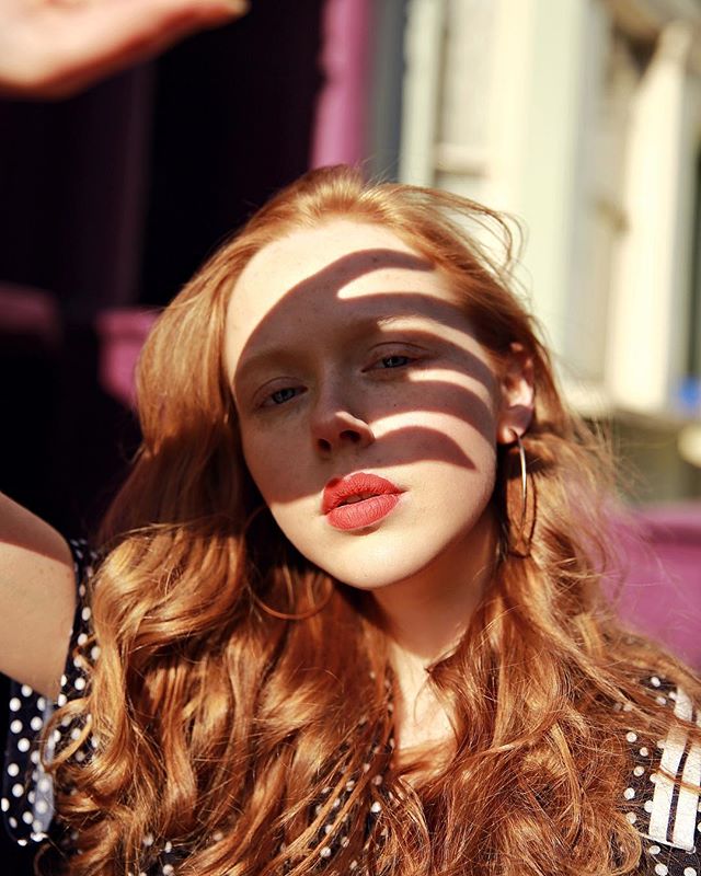 Portrait of a redhead woman with shadows on her face in a polka dot dress.
