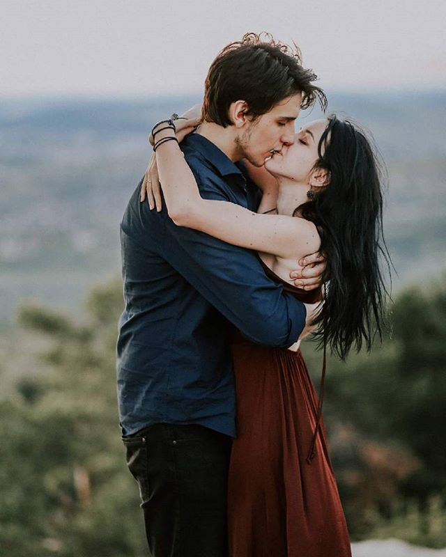 A loving couple embraces and shares a tender kiss amidst a scenic natural backdrop.