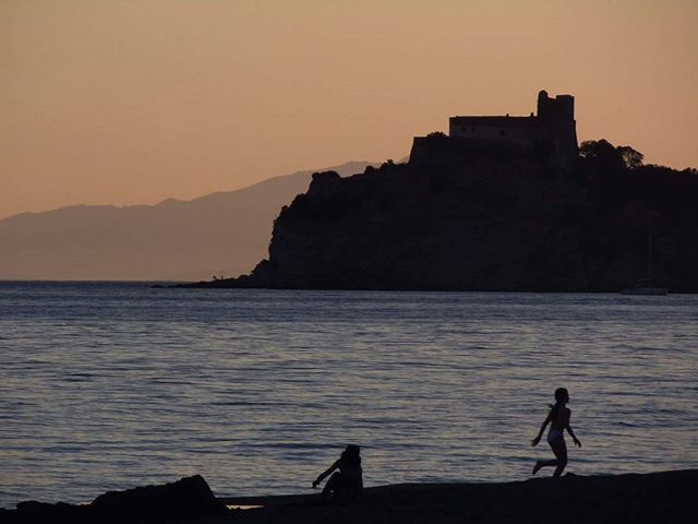 A scenic view of children playing on the beach with a castle silhouetted against the sunset sky.