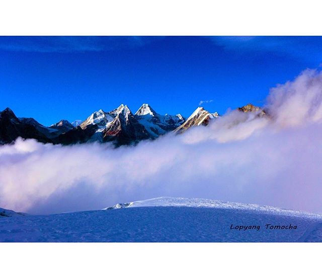 Majestic snow-capped mountains pierce through a sea of clouds under a clear blue sky.