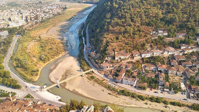 Aerial view of a European town with a river, bridge, and traditional buildings on a hillside.