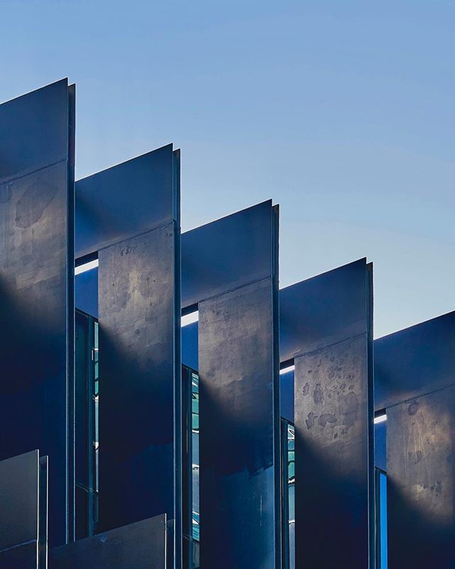 Abstract view of a modern building facade with geometric metal panels against a clear blue sky.