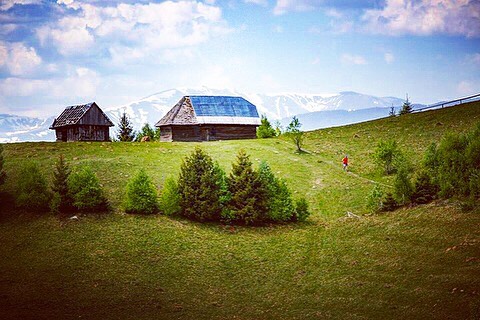 Scenic landscape featuring houses on a green hillside with majestic mountains in the background under a cloudy sky.