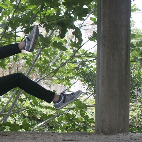Person wearing sneakers dangling their legs outdoors in a natural setting near a concrete structure.