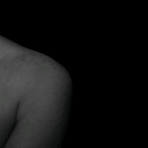 A close-up shows a shoulder against a dark backdrop for a vintage mood.