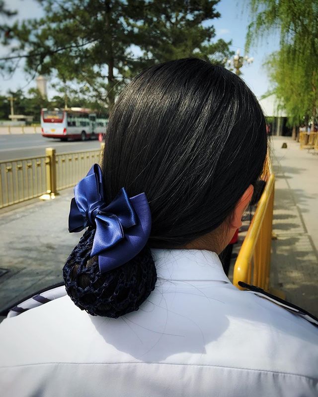 A woman with dark hair wears a navy bow and hairnet in a public outdoor setting.
