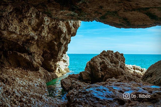 Seascape view from a coastal cave opening overlooking the turquoise ocean and rocky formations.