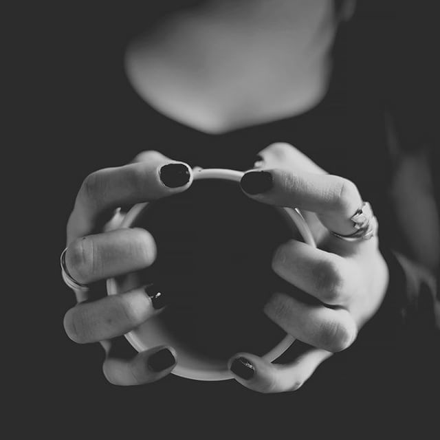 Close-up of hands holding a cup of coffee in black and white, creating a cozy and intimate scene.