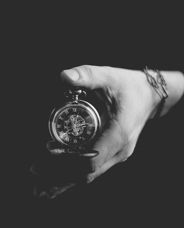 A close-up of a hand holding a vintage pocket watch against a dark background.
