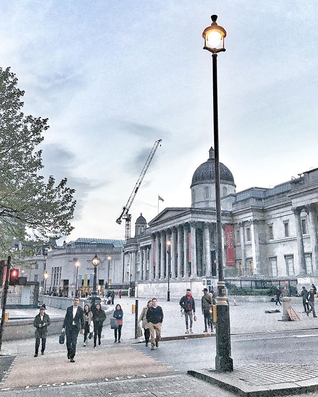People cross the street at a zebra crossing in an urban London scene with the National Gallery in the background.