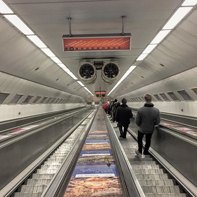 People ride down an escalator in a modern subway station, showcasing public transportation.