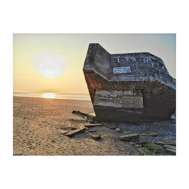 A concrete bunker stands on a beach during sunset, capturing a moment of history and tranquility.
