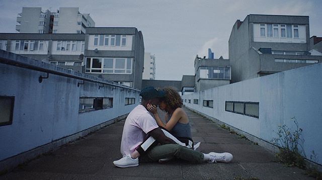 A couple embraces intimately on a rooftop with an urban cityscape as a backdrop.