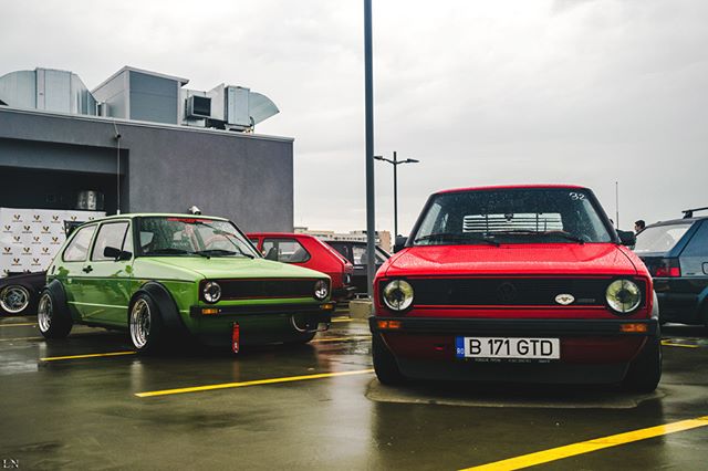 A green and red vintage VW Golf car are parked in a parking lot at a car meet.
