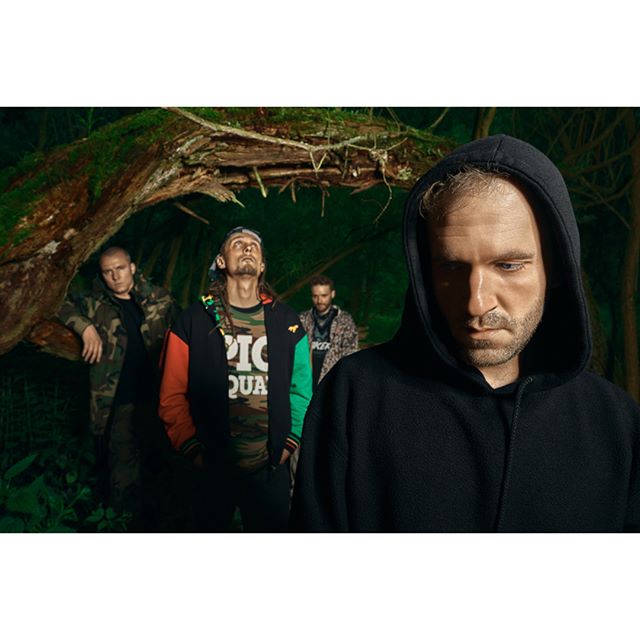 Group of men in hoodies standing in a forest.