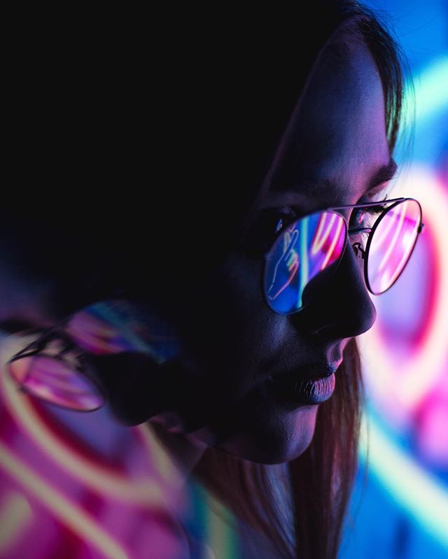A woman with sunglasses reflects neon lights in a modern, moody and intense atmosphere.